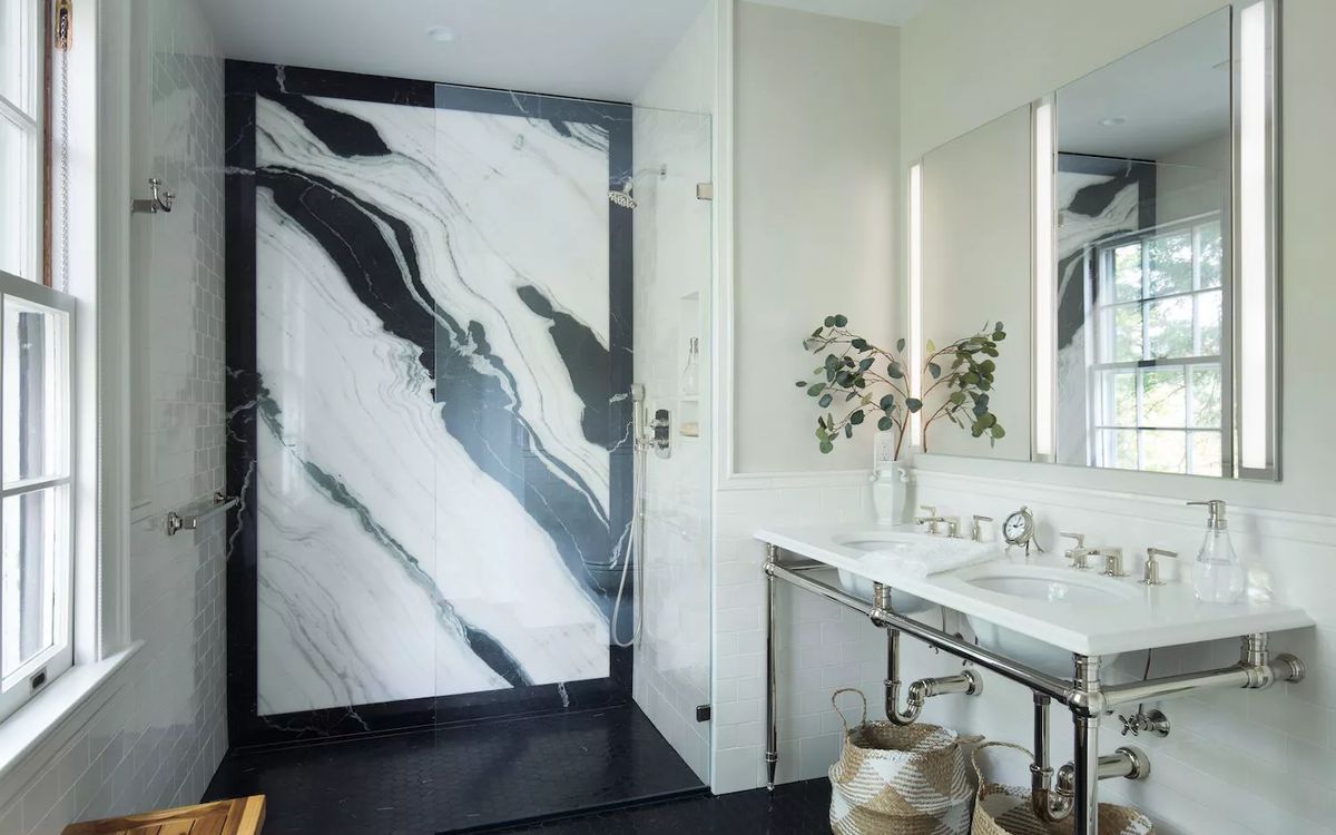 A remodeled bathroom with a glass walk-in shower, marble walls and a double vanity